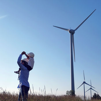 Man with child on his shoulders in a windmill field
