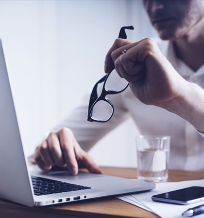 Man holding glasses while working on computer